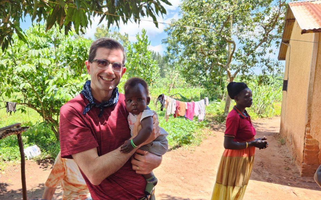 Jake holding a baby in Uganda. The baby's mother is in the background.