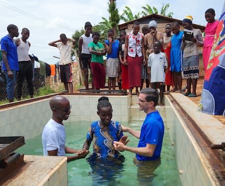 Two men baptize a woman with a crowd of onlookers.